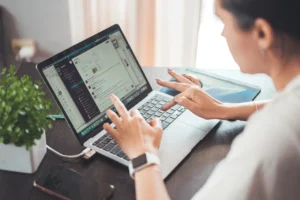 Mulher usando laptop em ambiente de trabalho com foco em produtividade digital, rodeada de objetos de escritório, incluindo uma planta.