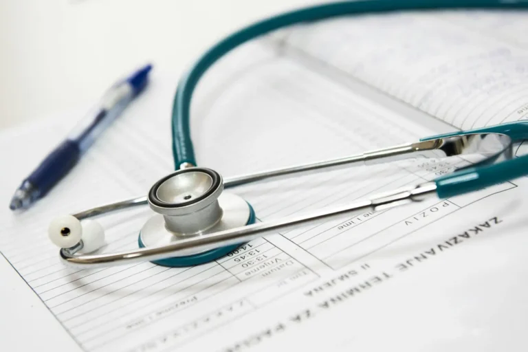 Imagem de um estetoscópio sobre um prontuário médico, com caneta azul e uma agenda ao fundo. Cena relacionada à saúde, medicina e cuidados médicos.