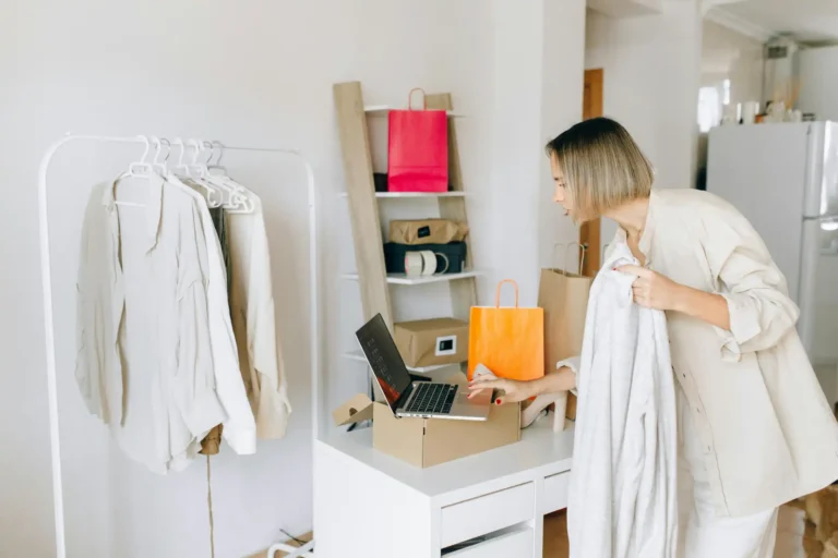 Mulher organizando roupas e compras online em ambiente doméstico, usando laptop e checklist. Cena de rotina de compras e organização em casa.