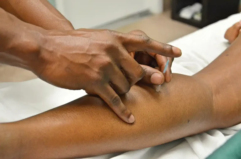 Profissional de saúde aplicando injeção em uma perna de paciente, atenção e cuidado durante procedimento médico.
